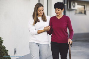 Dame met wandelstok die geholpen wordt door een jonge persoon in een woonzorgcentrum te Evergem in Meetjesland